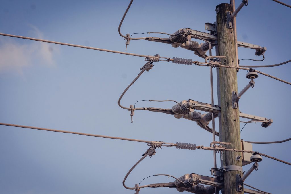 Wood utility pole with power line hardware and insulators against a blue sky.