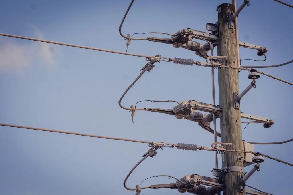 Wood utility pole with power line hardware and insulators against a blue sky.